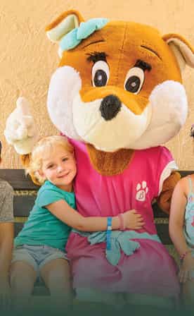 Trois jeunes enfants sourient en étant assis à côté de Léa, la grande peluche mascotte des clubs Belambra