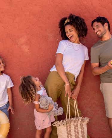 Adultes et enfants devant un mur terracotta à Belgodère, avec une bouée, une raquette et un sac de plage.