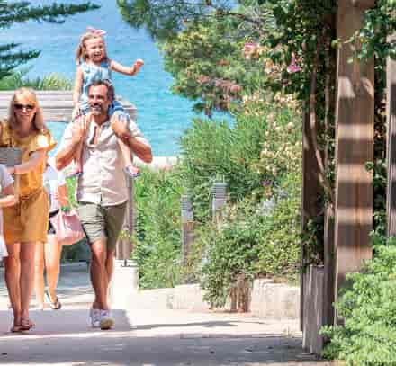 Famille rejoignant la plage à pied par les jardins du club Belgodère Belambra en bord de mer.