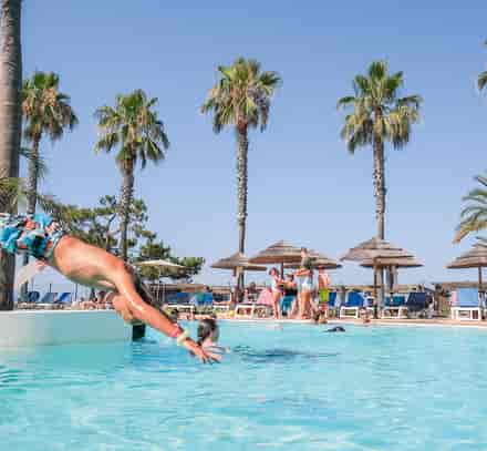 Enfant plongeant dans la piscine extérieure du club Belambra Borgo Pineto sous les palmiers.