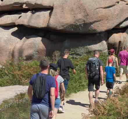 Un groupe de randonneurs marche au pied de grands rochers de granit rose sur le littoral breton.