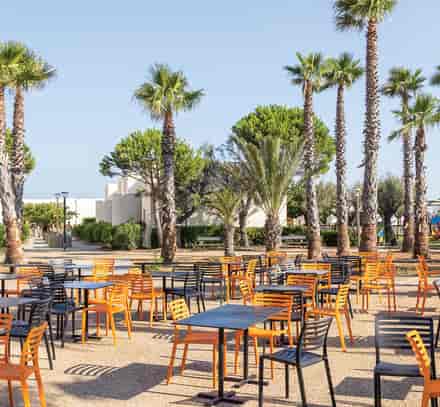 Terrasse avec tables et chaises colorées sous les palmiers au club Belambra à Gruissan.