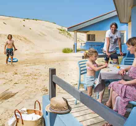 Une famille sur la terrasse d’un hébergement bleu face aux dunes à Seignosse.