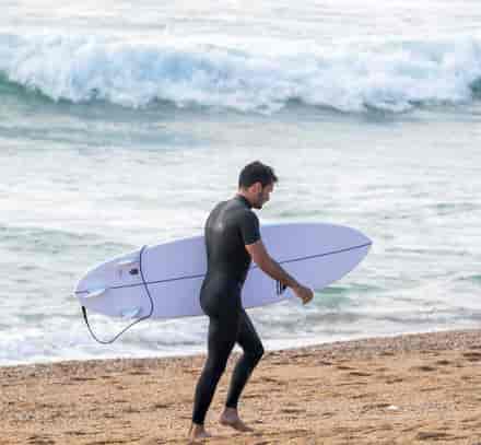 Surfeur rejoignant la plage avec sa planche face aux vagues de l'océan.