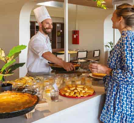 Vacancière se servant au buffet avec un chef dans le restaurant du club Belambra Anglet « La Chambre d'Amour ».
