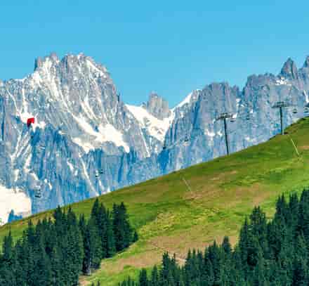 Panorama de sommets rocheux et enneigés au-dessus d’un versant boisé.