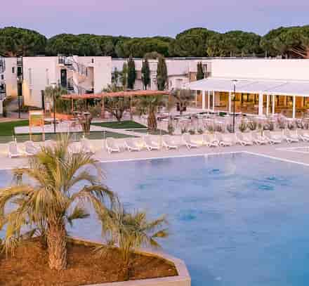 Vue sur les piscines et les bâtiments du club Belambra à Port Camargue avec un palmier au premier plan.