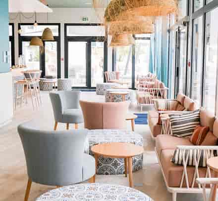 Salon avec fauteuils et tables basses près des grandes fenêtres au club Belambra à Port Camargue.